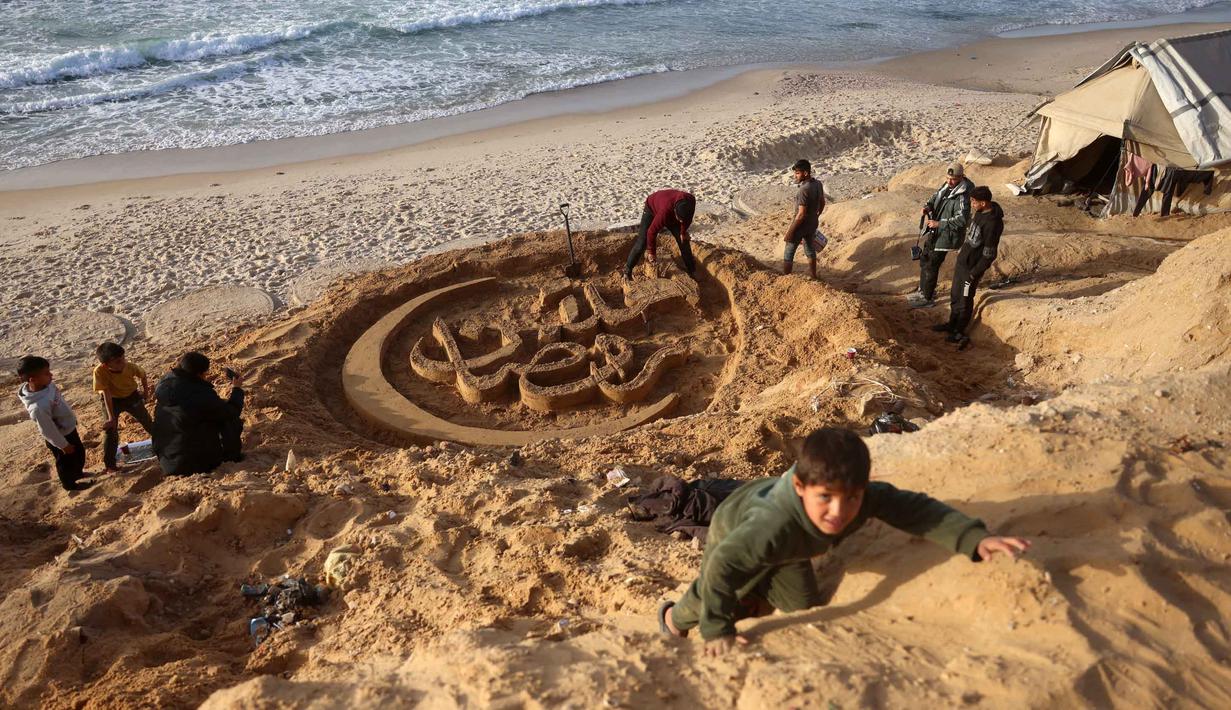 Hal tersebut dilakukan Yazeed Abu Jarad untuk menarik perhatian dunia terhadap situasi di Gaza saat memasuki tahun baru. Tampak dalam foto, seorang anak memanjat bukit pasir di depan patung pasir dengan pesan ucapan "Selamat Datang, Ramadan" yang dibuat oleh seniman Palestina, Yazeed Abu Jarad, di sepanjang pantai di Khan Younis, selatan Gaza pada 17 Februari 2026. (Bashar Taleb/AFP)