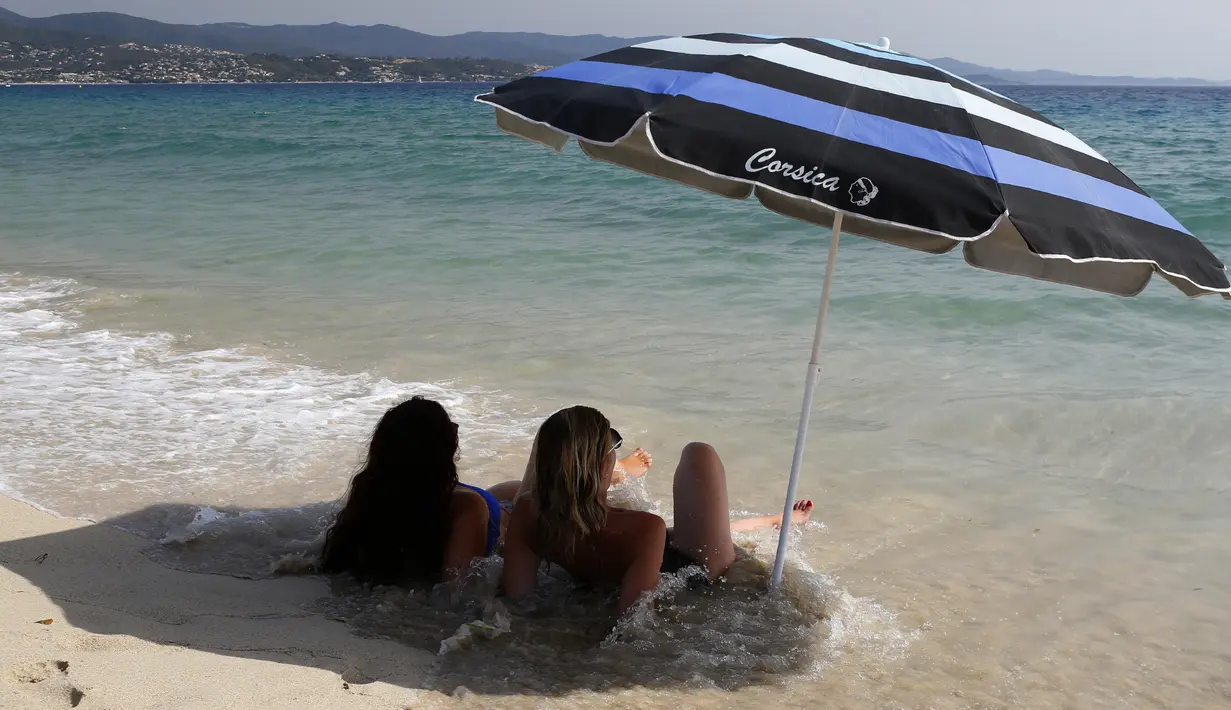 Dua wanita duduk di bawah payung di pantai Ricanto di Ajaccio, di pulau Corsica, Mediterania Prancis, (1/8). Suhu udara di Corsica telah mencapai 40 C (104 F). (AFP Photo/Pascal Pochard Casabianca)