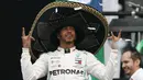 Pembalap Mercedes dari Inggris, Lewis Hamilton mengenakan topi sombrero merayakan keberhasilannya menjuarai balapan GP Meksiko di Autodromo Hermanos Rodriguez, Mexico City (28/10/2019). Kemenangan ini mendekatkan Hamilton ke titel juara dunia F1 2019. (AP Photo/Rebecca Blackwell)