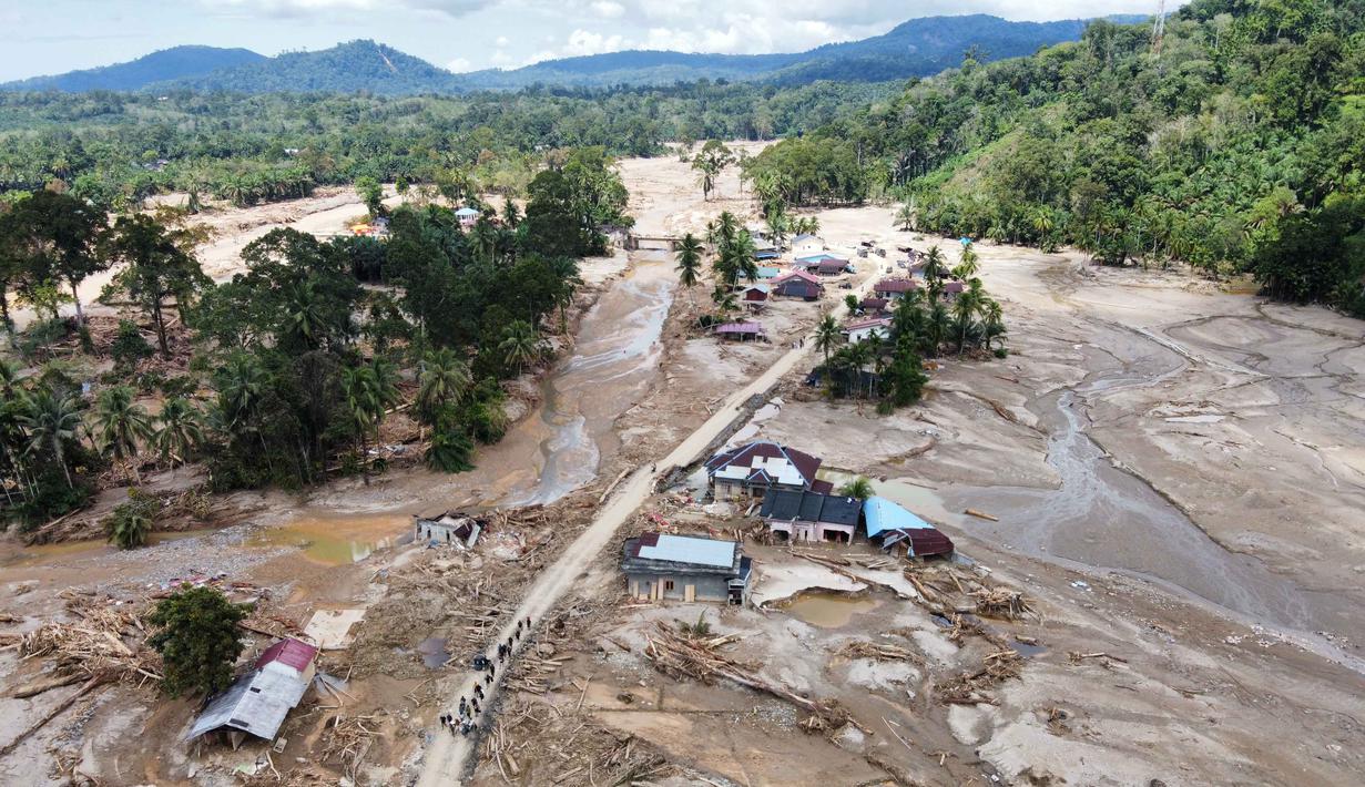 Warga berjalan di sepanjang jalan di sebuah desa yang terdampak banjir bandang di Batang Toru, Sumatera Utara, Senin 1 Desember 2025. Serangkaian bencana hidrometeorologi, yang mencakup banjir bandang (flash floods) dan tanah longsor dalam skala masif, menghantam beberapa wilayah di tiga provinsi di pulau Sumatera. (AP Photo/Binsar Bakkara)
