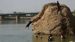 Anak-anak terjun dari reruntuhan bangunan tua ke Sungai Tigris untuk mendinginkan diri dari cuaca panas di Baghdad, Irak, Kamis (1/7/2021). Pemerintah Irak menetapkan 1 Juli 2021 sebagai hari libur resmi di Baghdad karena gelombang panas yang menyengat. (AP Photo/Khalid Mohammed)