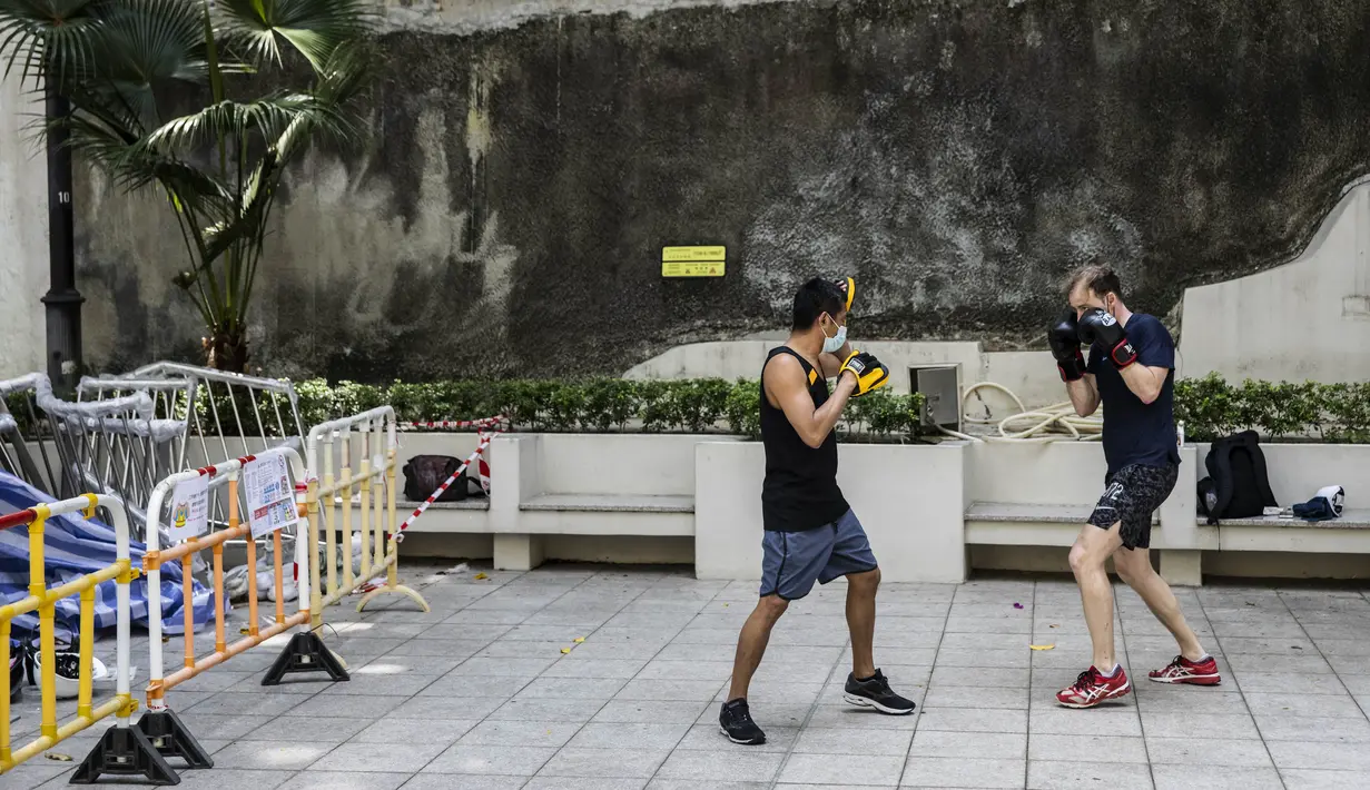 Dua pria berolahraga saat pemerintah mengumumkan pelonggaran pembatasan Covid-19 paling ketat di Hong Kong, Kamis (14/4/2022). Pelonggaran tersebut memungkinkan salon kecantikan, bioskop, dan pusat kebugaran dibuka kembali mulai 21 April 2022 mendatang. (ISAAC LAWRENCE/AFP)