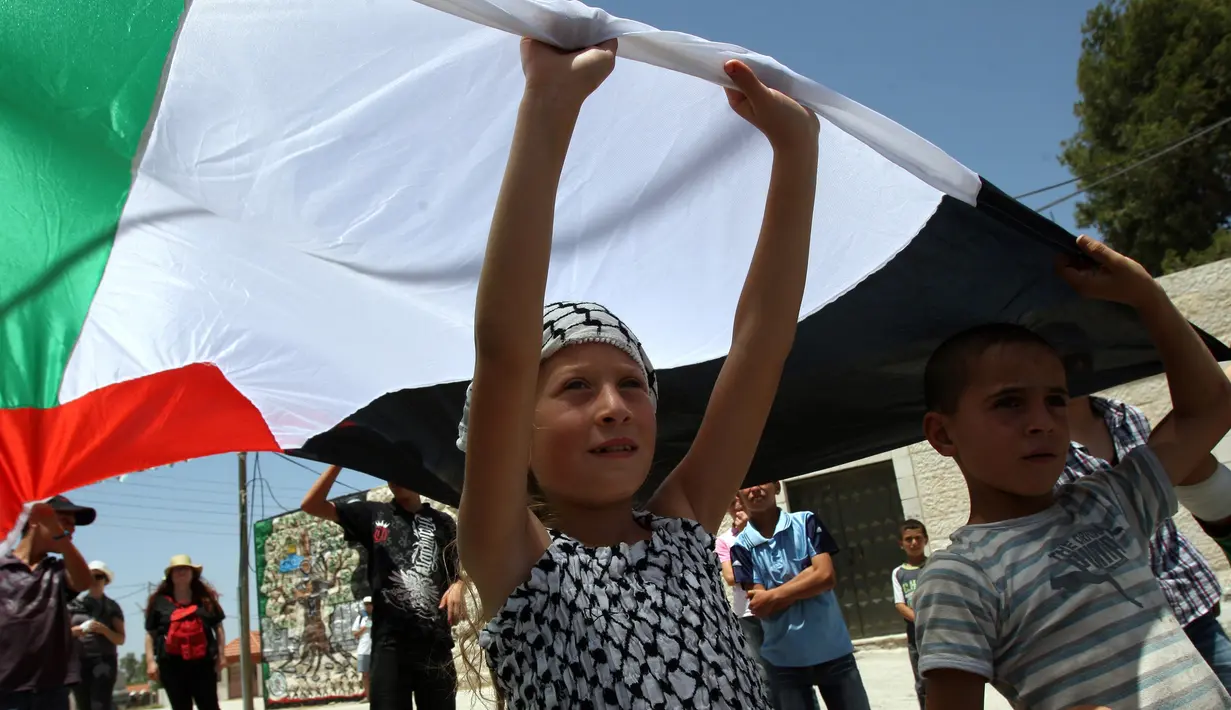 Foto yang diambil pada 10 Juni 2011 menunjukkan Ahed Tamimi memegang bendera nasional Palestina saat melakukan demonstrasi di Desa Nabi Saleh. Bagi keluarga Tamimi bukan kali ini saja mereka ditangkap oleh tentara Israel. (AFP Photo/Abbas Momani)