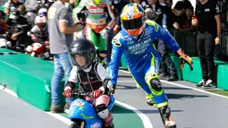 Pembalap MotoGP Alex Rins membantu seorang anak laki-laki mengendarai motor listrik mini saat acara jumpa pers jelang MotoGP Jepang di sirkuit Twin Ring Motegi, Jepang (12/10). (AP Photo / Shizuo Kambayashi)