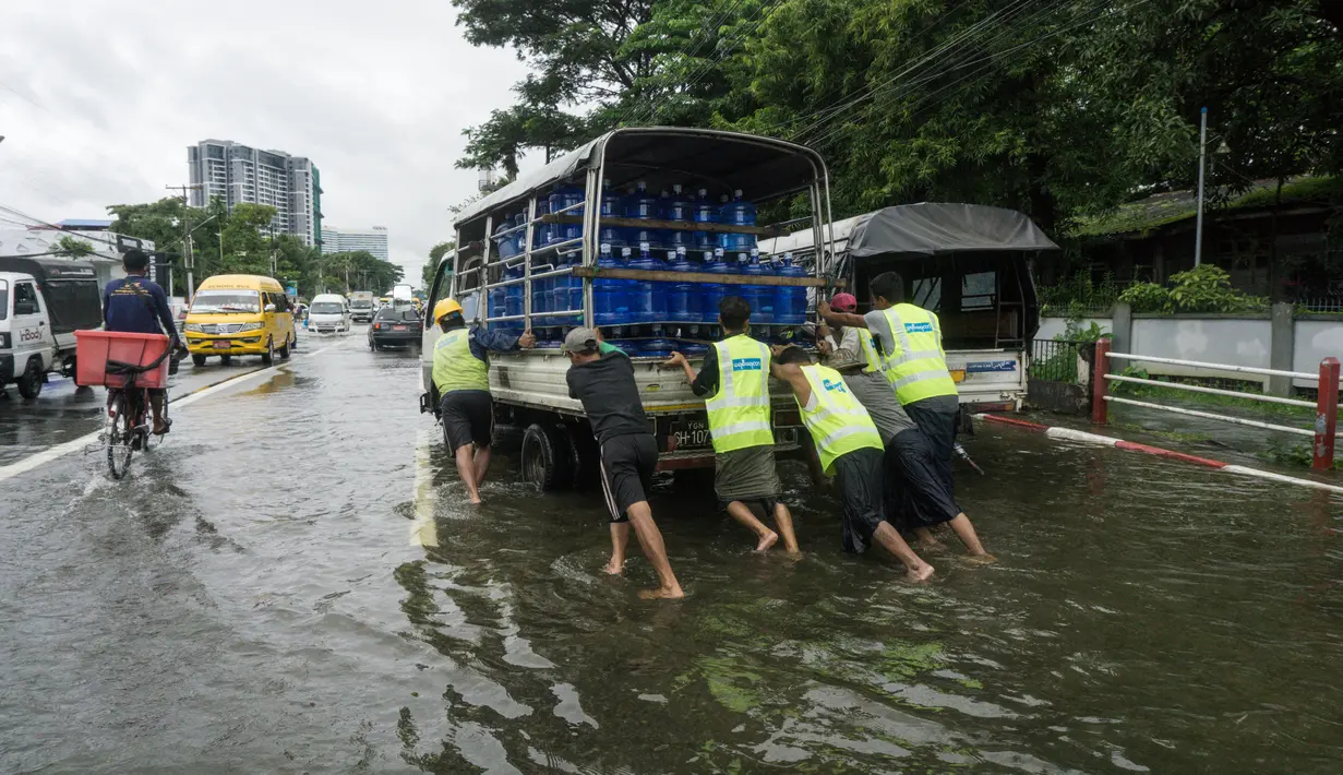 Orang-orang mendorong kendaraan yang mogok di jalan yang banjir di pinggiran Yangon, Myanmar  (17/8/2022). Sebagian besar kotapraja di Yangon dilanda banjir yang menyebabkan kemacetan lalu lintas pada jam-jam sibuk. (AFP/Stringer)