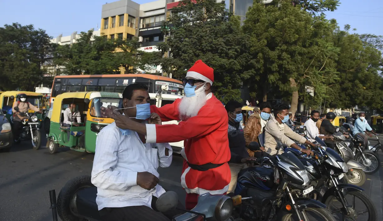 Pengguna jalan dipakaikan masker oleh presiden Angel Foundation dan pekerja sosial, Rufas Christian yang berpakaian Sinterklas di persimpangan lalu lintas di Ahmedabad, India, Kamis (17/12/2020). Aksi itu sebagai bagian dari kampanye kesadaran melawan penyebaran COVID-19. (SAM PANTHAKY/AFP)