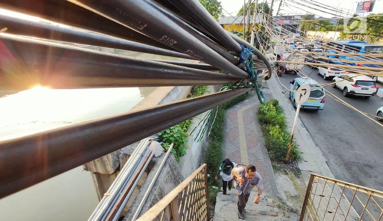 Pejalan kaki melintas dekat kabel semrawut di sekitar Jalan Gunung Sahari, Mangga Dua, Jakarta, Kamis (10/7/2019). Buruknya tata instalasi kabel di Ibu Kota menjadi penyebab banyaknya kabel semrawut, meskipun kondisi itu berbahaya serta mengganggu pemandangan. (Liputan6.com/Immanuel Antonius)