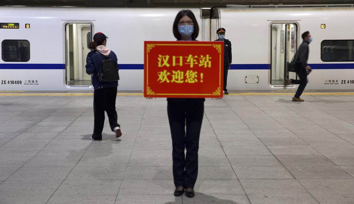 Petugas memegang papan bertuliskan ‘Stasiun Hankou menyambut Anda!’ saat para penumpang menaiki kereta pertama yang beroperasi usai berakhirnya lockdown akibat pandemi virus corona COVID-19 di Stasiun Hankou, Wuhan, Provinsi Hubei, China, Rabu (8/4/2020). (AP Photo/Ng Han Guan)