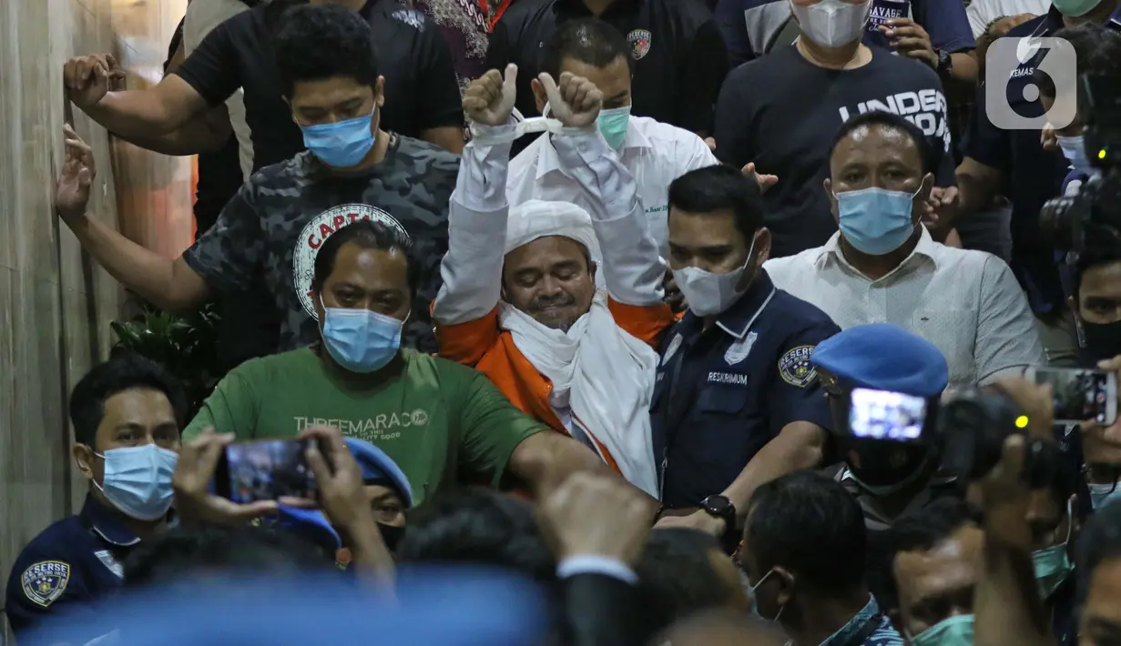 M Rizieq Shihab (tengah) mengangkat tangan saat meninggalkan gedung Ditreskrimum Polda Metro Jaya, Jakarta, Minggu dini hari (13/12/2020). Rizieq Shihab ditahan setelah menjalani pemeriksaan sebagai tersangka penghasutan dan kerumunan di tengah pandemi COVID-19. (Liputan6.com/Helmi Fithriansyah)