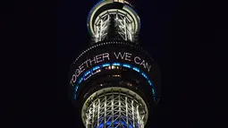 Menara Tokyo Skytree terlihat menyala dengan warna biru bertuliskan "Bersama Kita Semua Bisa Menang" di Tokyo, 5 April 2020. Ungkapan dukungan dan pesan harapan tersebut muncul di tengah merebaknya pandemi virus corona Covid-19. (CHARLY TRIBALLEAU/AFP)
