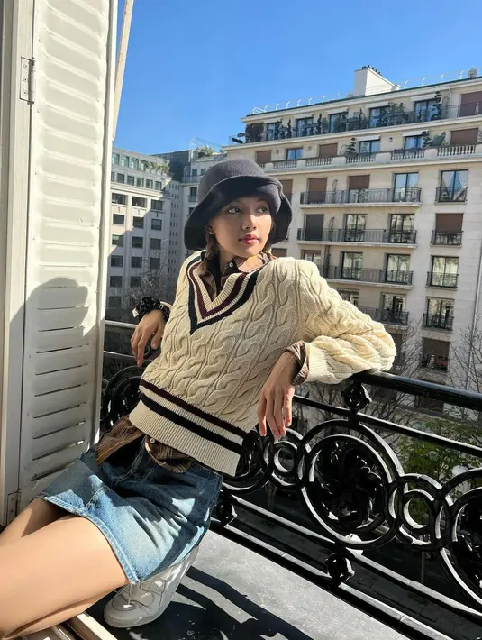 Momen Lisa di Paris, berpose di pinggir jendela kamar hotelnya dengan outfit bernuansa preppy. Kemeja cokelat ditumpuknya dengan sweater dan dipadu dengan mini skirt jeans. Di sini, ia mengenakan bucket hat hitam. Foto: Instagram.