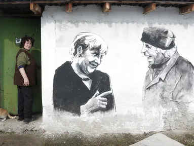 Ivanka Toneva memasuki halaman rumahnya di sebelah mural yang menggambarkan sang suami, Krustyo Tonev yang sedang berbincang dengan Kanselir Jerman, Angela Merkel, di desa Staro Zhelezare, Bulgaria, Kamis (27/7). (AP Photo/Valentina Petrova)
