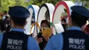 Polisi berjaga saat orang-orang berpose di depan cincin Olimpiade jelang upacara pembukaan Olimpiade Tokyo 2020 di luar Stadion Olimpiade, Tokyo, Jepang, Jumat (23/7/2021).  Upacara pembukaan Olimpiade Tokyo 2020 akan digelar pada 23 Juli 2021 malam. (Andrej ISAKOVIC/AFP)