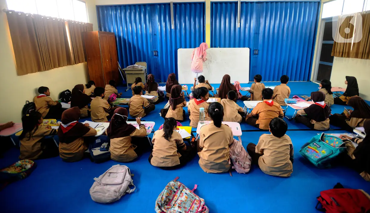 Seorang guru mengajar murid tanpa menggunakan meja dan kursi sekolah, di SDN Bojong Nangka 02, Kabupaten Bogor, Jawa Barat, Kamis (16/2/2023). Sudah lebih dari dua pekan, murid-murid di tiga ruang kelas  menerapkan kegiatan belajar mengajar beralas karpet karena belum tersedianya bangku dan meja. (merdeka.com/Arie Basuki)