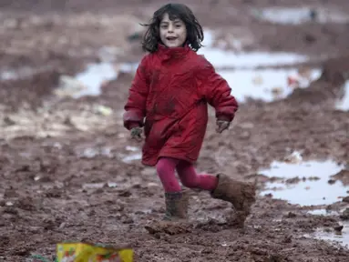 Seorang bocah pengungsi Suriah berlari di jalanan berlumpur di kamp pengungsi Bab Al-Salam, dekat perbatasan Suriah-Turki, Provinsi Aleppo Utara, Senin (26/12). Di sini tercatat sekitar ribuan warga yang telah lama hidup di tenda. (REUTERS/Khalil Ashawi)