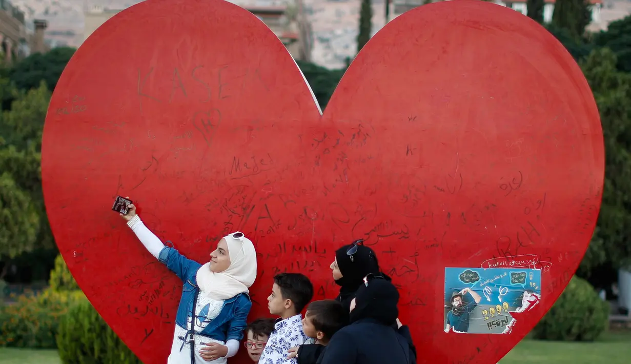 Seorang gadis Suriah menggunakan ponselnya berselfie dengan keluarganya dengan latar bentuk hati yang menggambarkan cinta untuk Damaskus, di Alun-alun Omayyid, Suriah, (18/7). (AP Photo / Hassan Ammar)