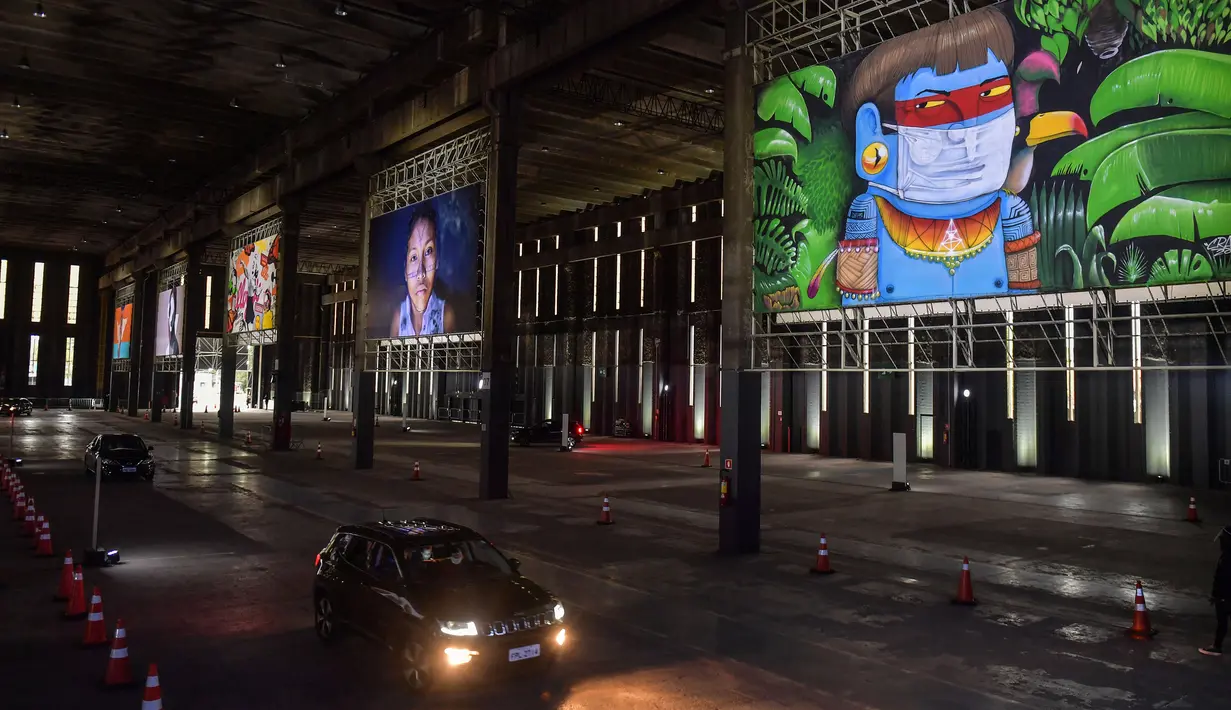Orang-orang mengunjungi pameran seni dengan mengendarai mobil mereka melintasi gudang yang memajang lukisan dan foto di Sao Paulo pada 30 Juli 2020. Dengan galeri-galeri dan museum ditutup akibat pandemi virus corona, pemilik galeri seni Brasil meresmikan pameran drive-thru. (NELSON ALMEIDA/AFP)