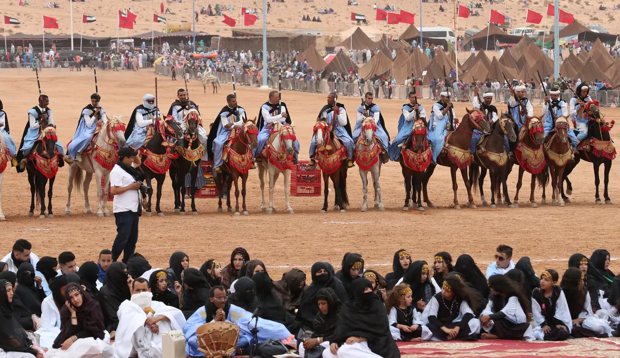 Penunggang kuda dan para wanita berkumpul dalam Festival Tan-Tan Moussem Berber ke-14 di Kota Tan-Tan, Maroko, Minggu (8/7). Festival ini untuk mempromosikan tradisi lokal dan menyatukan suku nomaden dari Afrika Utara. (KARIM SAHIB/AFP)
