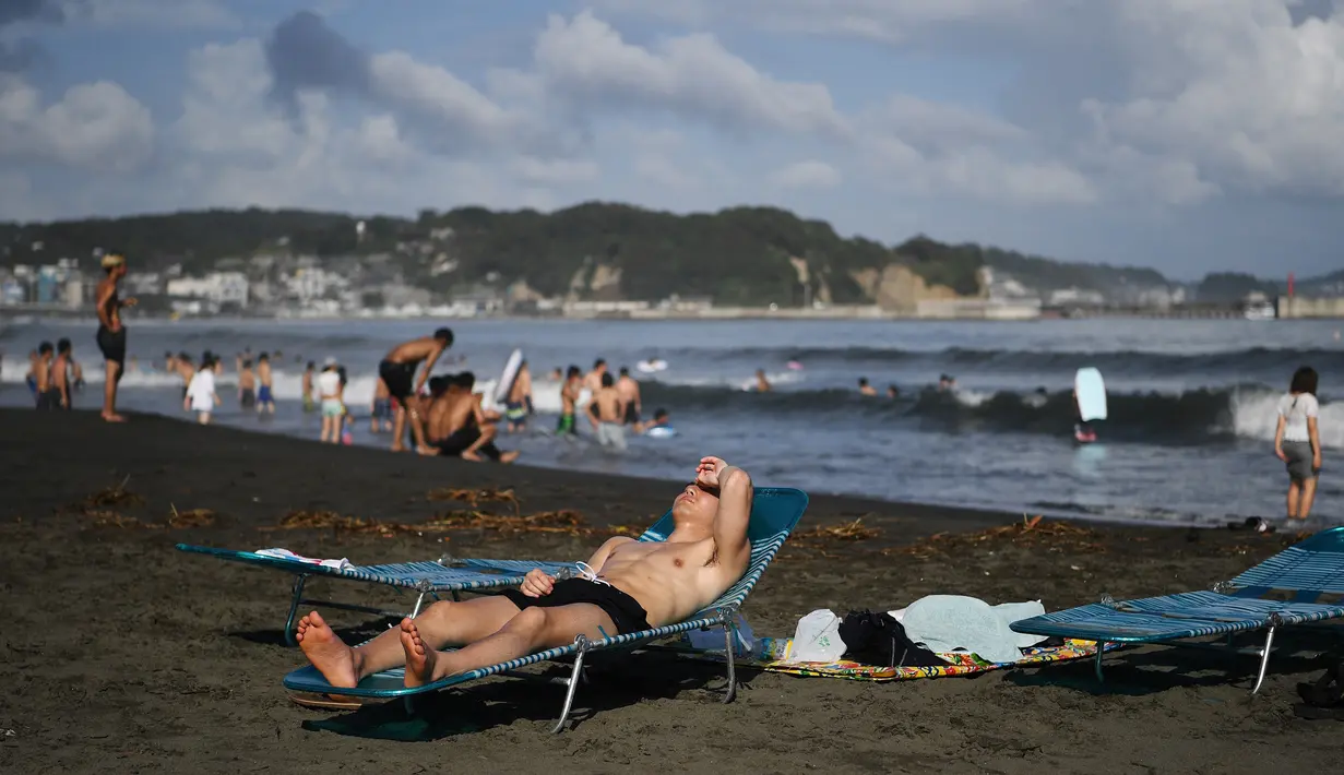 Seorang pria berjemur di sepanjang pantai dekat Pulau Enoshima di pantai Prefektur Kanagawa, barat daya Tokyo (13/8/2019). (AFP Photo/Charly Triballeau)