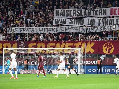 Suporter FC Metz membentangkan spanduk bertulisakan "Pemenang derby Kaiserlautern, kami berada di final" untuk mendukung FC Kaiserlautern yang mencapai final Piala DFB Pokal pada laga lanjutan Liga Prancis 2023/2024 melawan RC Lens di Saint-Symphorien Stadium, Longeville-les-Metz, Prancis, Sabtu (13/04/2024) dini hari WIB. (AFP/Jean-Christophe Verhaegen)