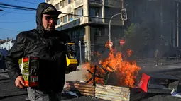 Seorang penjarah berlari melewati api unggun selama protes di Valparaiso, Chile, Minggu (20/10/2019). Bentrokan pecah di Santiago setelah dua orang tewas ketika sebuah supermarket dibakar ketika protes terhadap kondisi ekonomi dan ketidaksetaraan sosial. (JAVIER TORRES/AFP)