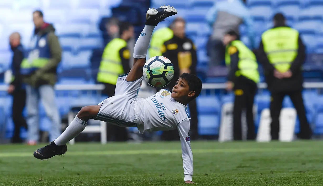 Putra dari Cristiano Ronaldo melakukan tendangan salto saat menemani sang ayah di Stadion Santiago Bernabeu, Madrid, Minggu (8/4/2018). Tendangan ini mirip seperti saat CR 7 membobol gawang Juventus. (AFP/Gabriel Bouys).