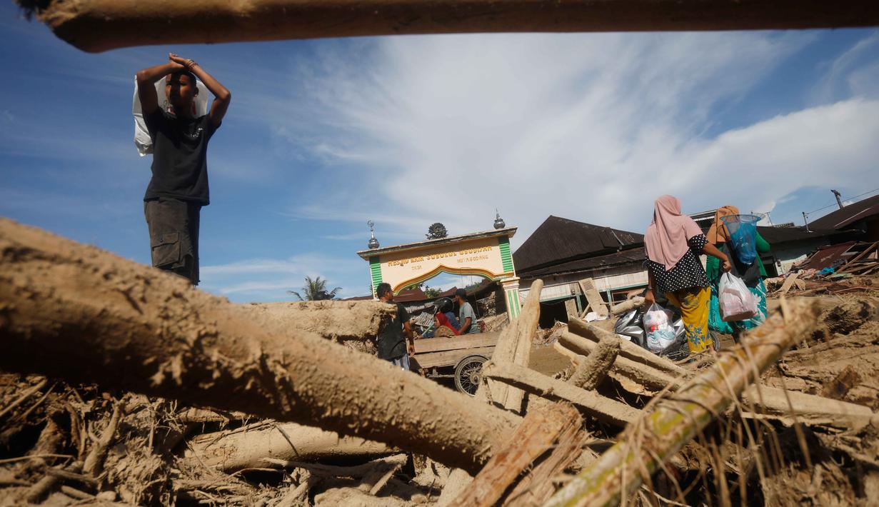 Selain rumah warga terdampak, kayu-kayu gelondongan juga masih terlihat tertumpuk di sepanjang aliran Sungai Aek Garoga dan Sungai Batang Toru. Tampak dalam foto, para penyintas berjalan melewati tumpukan kayu yang tersapu banjir bandang di Batang Toru, Sumatra Utara, Selasa 2 Desember 2025. (AP Photo/Binsar Bakkara)