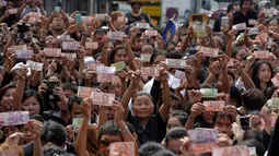 Rakyat Thailand memperlihatkan uang bergambar Raja Thailand Bhumibol Adulyadej saat menunggu pemindahan jenazah Bhumibol dari rumah sakit menuju Grand Palace, Bangkok, Thailand, Jumat (14/10). (REUTERS / Chaiwat Subprasom)