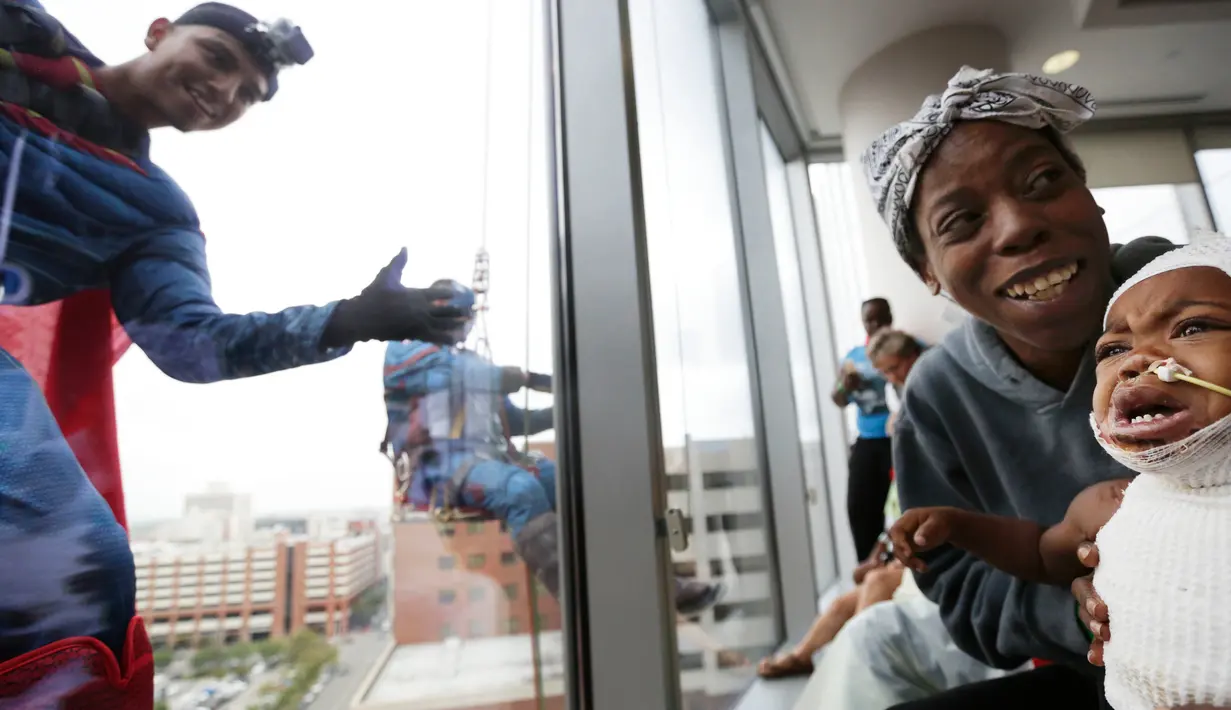 Pasien anak bereaksi saat superhero Superman melambaikan tangan di jendela sebuah rumah sakit di Birmingham, Rabu (11/10). Sekelompok superhero bekerja membersihkan jendela rumah sakit untuk menghibur anak- anak yang sedang sakit (AP Photo/Brynn Anderson)