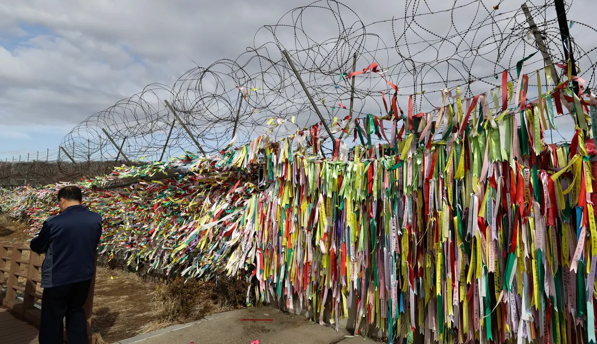 Seorang pria berjalan di dekat pagar kawat yang dihiasi ribuan pita bertuliskan pesan damai antara Korea Selatan dan Korea Utara di Paviliun Imjingak, Paju, Korea Selatan, Senin (5/3). (AP Photo/Lee Jin-man)