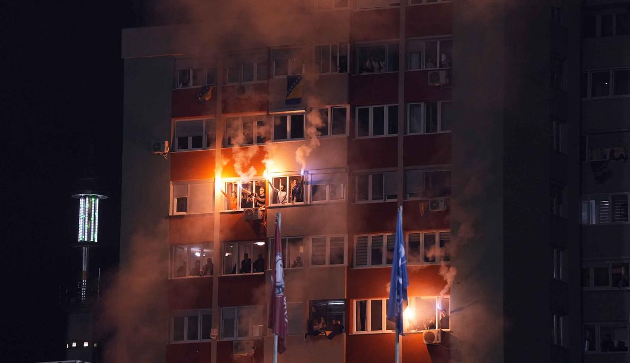 Kepastian ini didapat usai membungkam Italia pada final play-off kualifikasi Piala Dunia 2026 zona Eropa. Tampak dalam foto, suporter Timnas Bosnia dan Herzegovina menyalakan suar saat mereka menyaksikan pertandingan final play-off kualifikasi Piala Dunia 2026 zona Eropa melawan Italia dari sebuah gedung apartemen tepat di luar stadion, Zenica, Bosnia, Selasa, 31 Maret 2026. (Fabio Ferrari/LaPresse via AP)