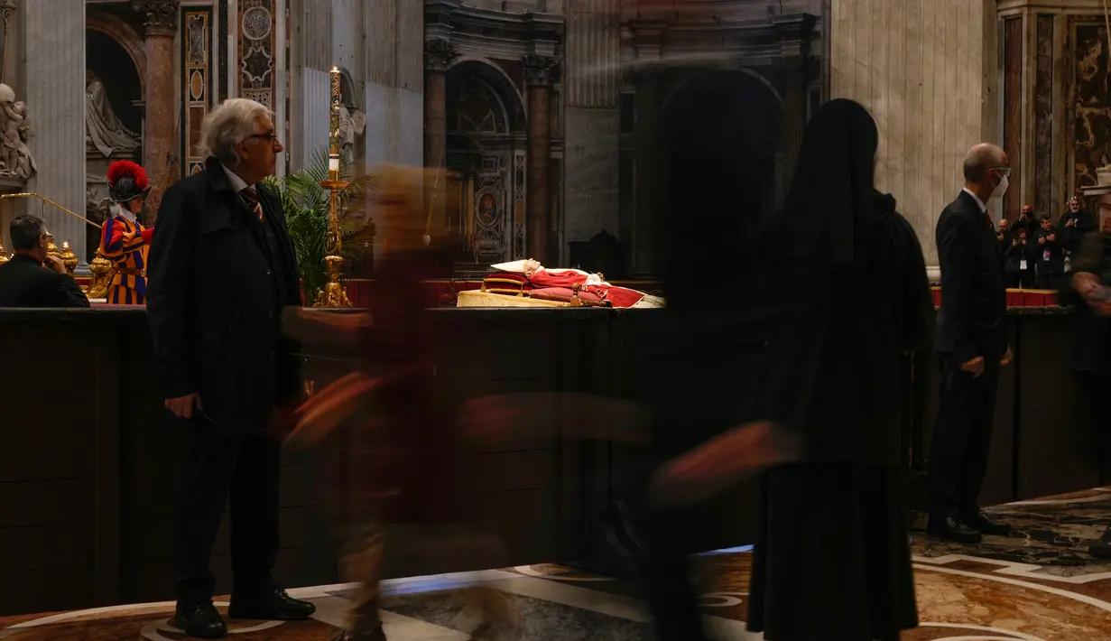 Orang-orang melihat jenazah mendiang Paus Emeritus Benediktus XVI yang disemayamkan di Basilika Santo Petrus, Vatikan, Senin (2/1/2023). Benediktus XVI, teolog Jerman yang akan dikenang sebagai paus pertama dalam 600 tahun yang mengundurkan diri, telah meninggal pada 31 Desember 2022 di usia 95 tahun. (AP Photo/Andrew Medichini)