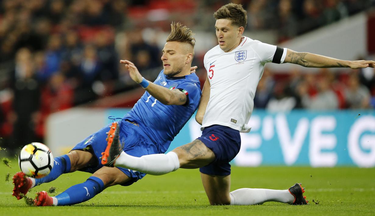 Pemain Italia, Ciro Immobile (kiri) berebut bola dengan pemain Inggris,  John Stones pada laga uji coba di Wembley Stadium, London, (27/3/2018). Italia tahan imbang Inggris 1-1. (AP/Alastair Grant)
