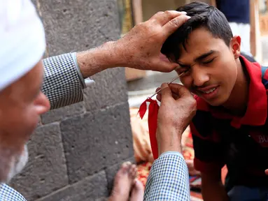 Seorang pria Yaman mengoleskan kosmetik tradisional kohl ke kelopak mata pria lain di Masjid Agung, kota tua Sanaa pada 9 mei 2019. Bagi muslim Yaman, pemakaian kohl diyakini mampu membersihkan dan melindungi mata dari penyakit ini sudah menjadi tradisi setiap bulan Ramadan. (MOHAMMED HUWAIS/AFP)