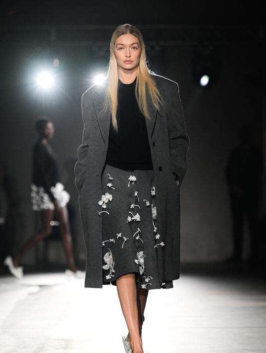 Gigi Hadid berjalan di catwalk saatmempersembahkan kreasi Prada selama Koleksi Wanita Musim Gugur-Musim Dingin 2023-2024 sebagai bagian dari Fashion Week di Milan pada 23 Februari 2023. Model asal AS itu tampil sangat stylish dalam balutan jas panjang abu-abu berlapis di atas jumper hitam dan mengenakan sepasang celana pendek abu-abu panjang yang unik, dihiasi dengan bunga putih tiga dimensi yang halus. (AFP/Marco Bertorello)