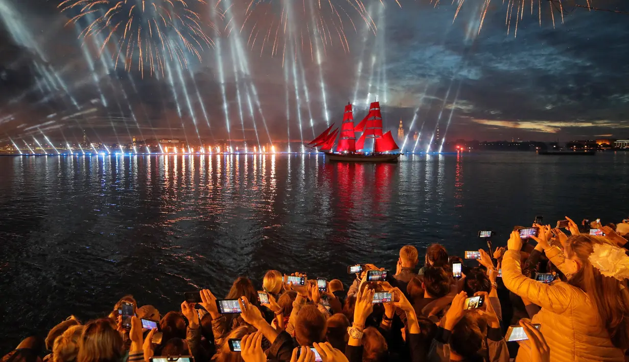 Orang-orang menonton kembang api dan perahu berlayar merah saat White Nights Festival di St.Petersburg, Rusia (24/6). Tradisi ini dimulai di akhir Perang Dunia Kedua untuk memperingati berakhirnya tahun ajaran sekolah. (AP/Dmitri Lovetsky)