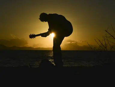 Seorang pria memainkan gitar saat matahari terbenam atau sunset di pantai Banda Aceh pada 28 Juni 2019. Pemandangan makin sempurna saat matahari tenggelam hingga alam berubah semakin remang dan romantis. (Photo by CHAIDEER MAHYUDDIN / AFP)
