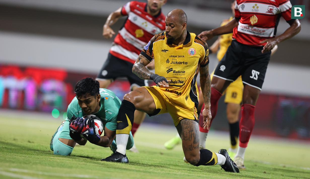 Pemain Persija Jakarta, Gustavo Almeida (kanan) berduel dengan kiper Madura United pada lanjutan BRI Super League 2025/2026 di Stadion Gelora Ratu Pamelingan, Jumat (24/10/2025) malam WIB. (Bola.com/Abdul Aziz).