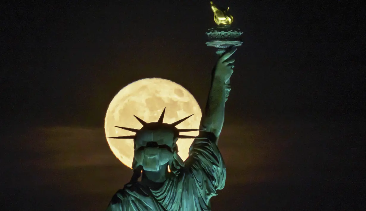 Bulan purnama muncul di depan Patung Liberty, New York, Amerika Serikat, 14 Juni 2022. Fenomena ini disebut juga sebagai Strawberry Supermoon karena terjadi pada saat panen strawberry. (AP Photo/J. David Ake)