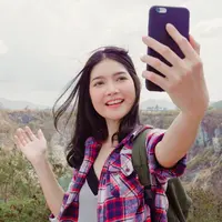 potret perempuan yang tersenyum sambil memegang ponsel dengan pemandangan pegunungan/copyright freepik.com/tirachardz
