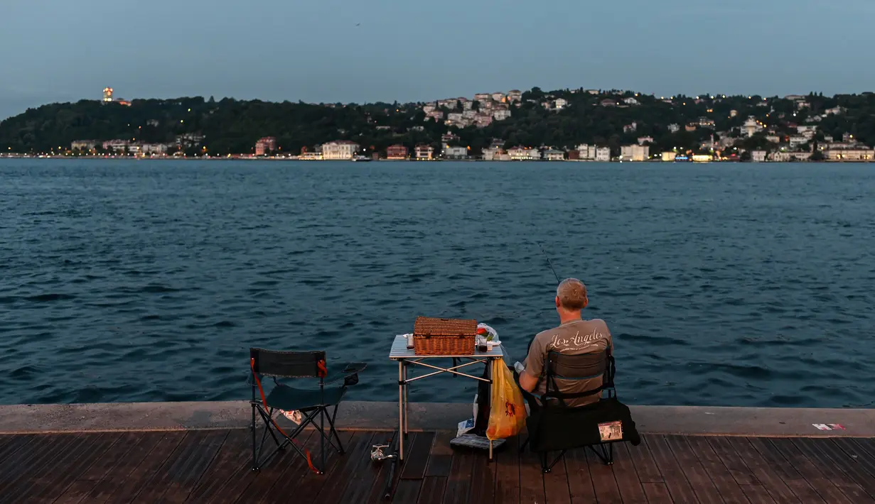 Orang-orang menikmati malam di sebelah pantai Bosphorus ketika jembatan Fatih Sultan Mehmet terlihat di Istanbul (6/7/2020). Ketika diselesaikan pada 1988, jembatan tersebut menjadi jembatan gantung terpanjang ke-5 di dunia; sekarang jembatan tersebut berada pada urutan ke-19. (AFP/Ozan Kose)
