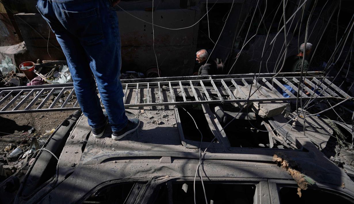 Serangan intensif Israel di wilayah Lebanon juga memicu pengungsian besar-besaran. Tampak dalam foto, seorang pria berdiri di atas mobil yang rusak sementara yang lain berjalan melewati puing-puing di lokasi serangan Israel pada Minggu 5 April 2026 terhadap sebuah bangunan di lingkungan Jnah, Beirut, Lebanon, Senin 6 April 2026. (AP Photo/Hassan Ammar)