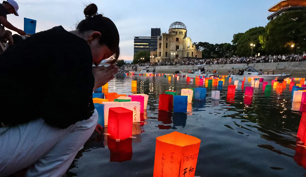 Foto yang diambil pada tanggal 6 Agustus 2024 ini menunjukkan seorang wanita yang sedang berdoa saat lentera dilepaskan ke Sungai Motoyasu, di seberang Kubah Bom Atom dekat Taman Peringatan Perdamaian di Hiroshima. (JIJI Press/AFP/Japan OUT)