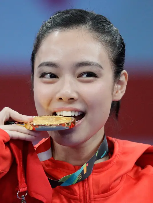 Atlet wushu Indonesia, Lindswell Lindswell menggigit medali emas usai memenangkan kategori wushu taijijian putri Asian Games 2018 di Jakarta, Senin (20/8). (AP Photo/Aaron Favila)