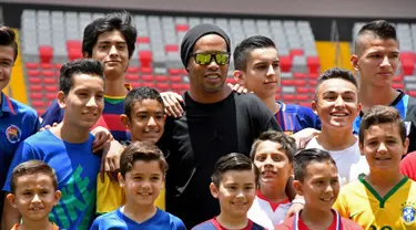 Mantan bintang sepak bola Brasil Ronaldinho berpose dengan anak-anak Kosta Rika sebelum pertandingan persahabatan melawan mantan pemain Kosta Rika di Stadion Nasional di San Jose, (4/8). (AFP Photo/Ezequiel Becerra)