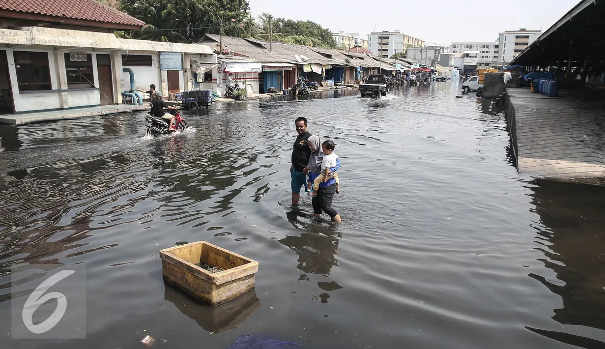 Warga melintasi genangan banjir di pasar ikan Pelabuhan Muara Baru, Penjaringan, Jakarta, (7/6). Banjir rob terjadi akibat jebolnya tanggul di sisi Timur Pelabuhan Muara Baru hingga meluapnya air yang mencapai sekitar 50 cm. (Liputan6.com/Faizal Fanani)