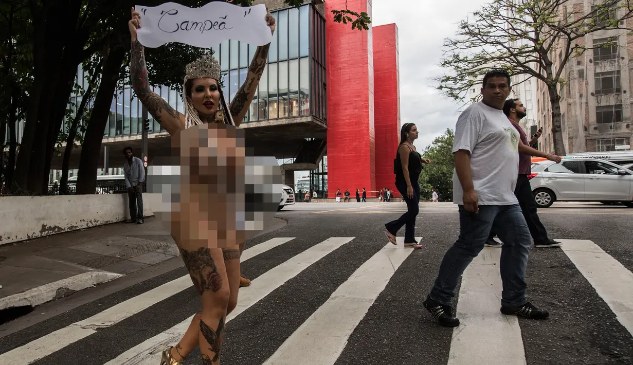 Pejalan kaki melihat aksi Sabrina Boing Boing dari sekolah Samba Tautape berjalan memegang poster bertuliskan "Juara" di Jalan Paulista, Sao Paulo, Brasil (2/3). Untuk pertam kalinya sejak 64 tahun sekolah Samba ini menang. (AFP Photo / Nelson Almeida)