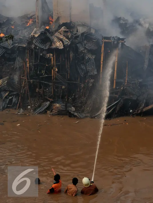 Petugas pemadam berupaya menyemprotkan air saat terjadinya kebakaran yang melanda rumah hunian semi permanen di bantaran sungai anak kali ciliwung, Kawasan Kampung Berland, Jakarta, Rabu (2/9/2015). (Liputan6.com/Johan Tallo)