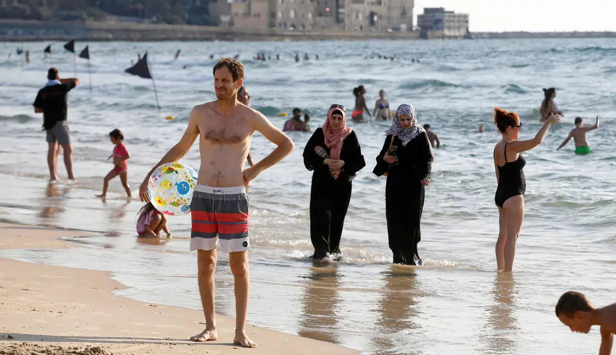 Dua orang wanita berjilbab berjalan di tepi pantai Laut Mediterania, Tel Aviv, Israel (30/8). Para wanita hijab ini tetap santai di tengah keramaian wanita berbikini. (REUTERS / Baz Ratner)