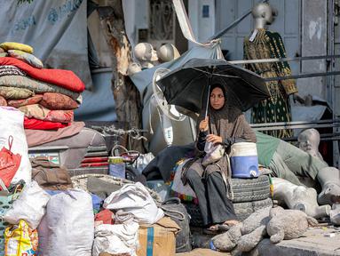 Seorang wanita duduk di samping barang-barang yang diselamatkan dari puing-puing Menara Prajurit Tak Dikenal di kawasan Rimal, Kota Gaza, pada 15 September 2025. (Omar AL-QATTAA/AFP)